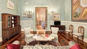 Une pièce avec un plancher en bois, une table basse au centre, deux fauteuils, un buffet et un téléviseur.