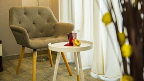 A room with a tufted armchair, a small round table with a glass, and a plant. - Santamaria Inn (Rome)