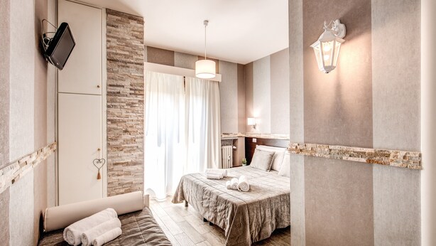 A hotel room with a bed, a desk, a chair, a TV, and a wall-mounted light fixture. - Santamaria Inn (Rome)