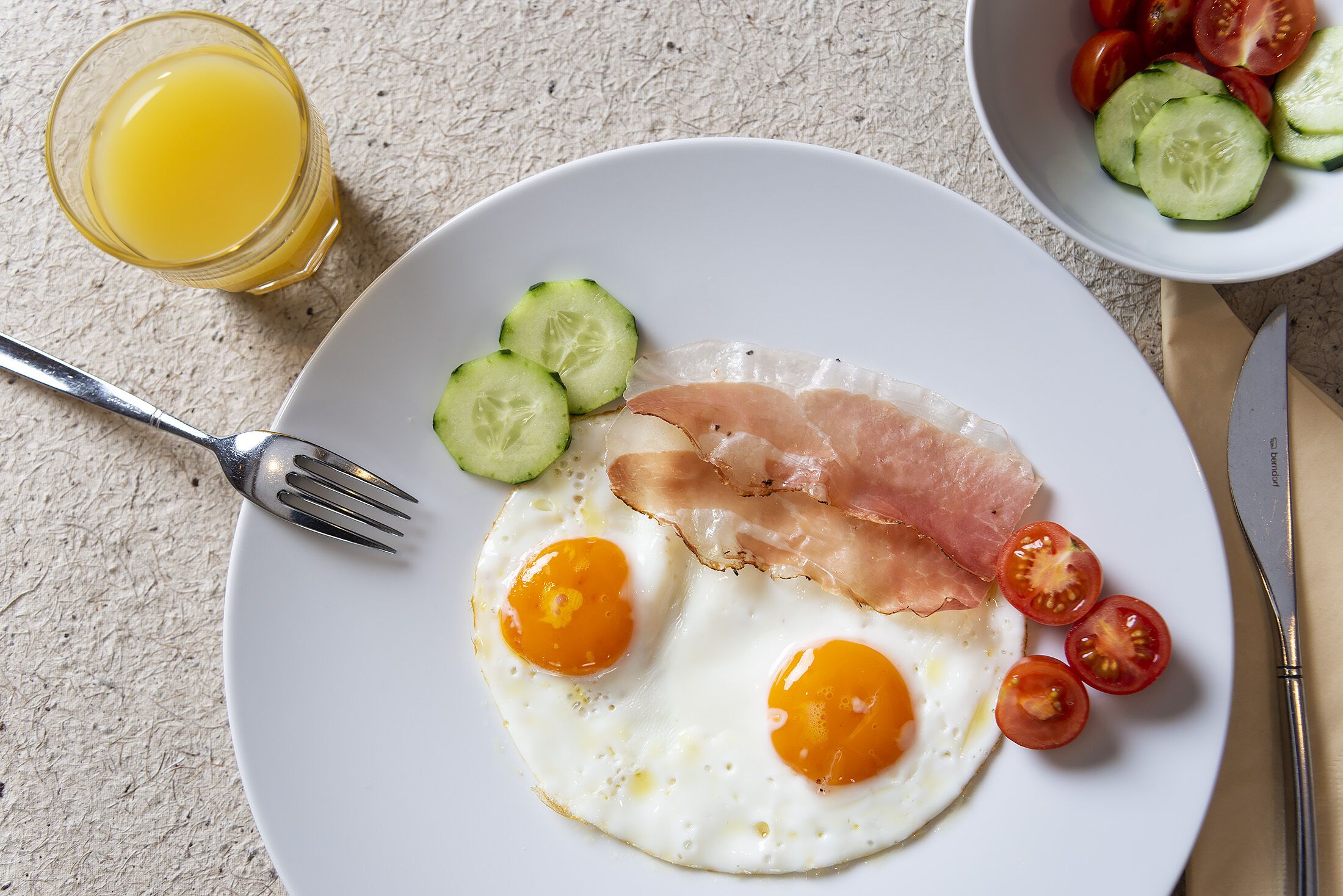 A breakfast plate with eggs, ham, and tomatoes on a white plate.