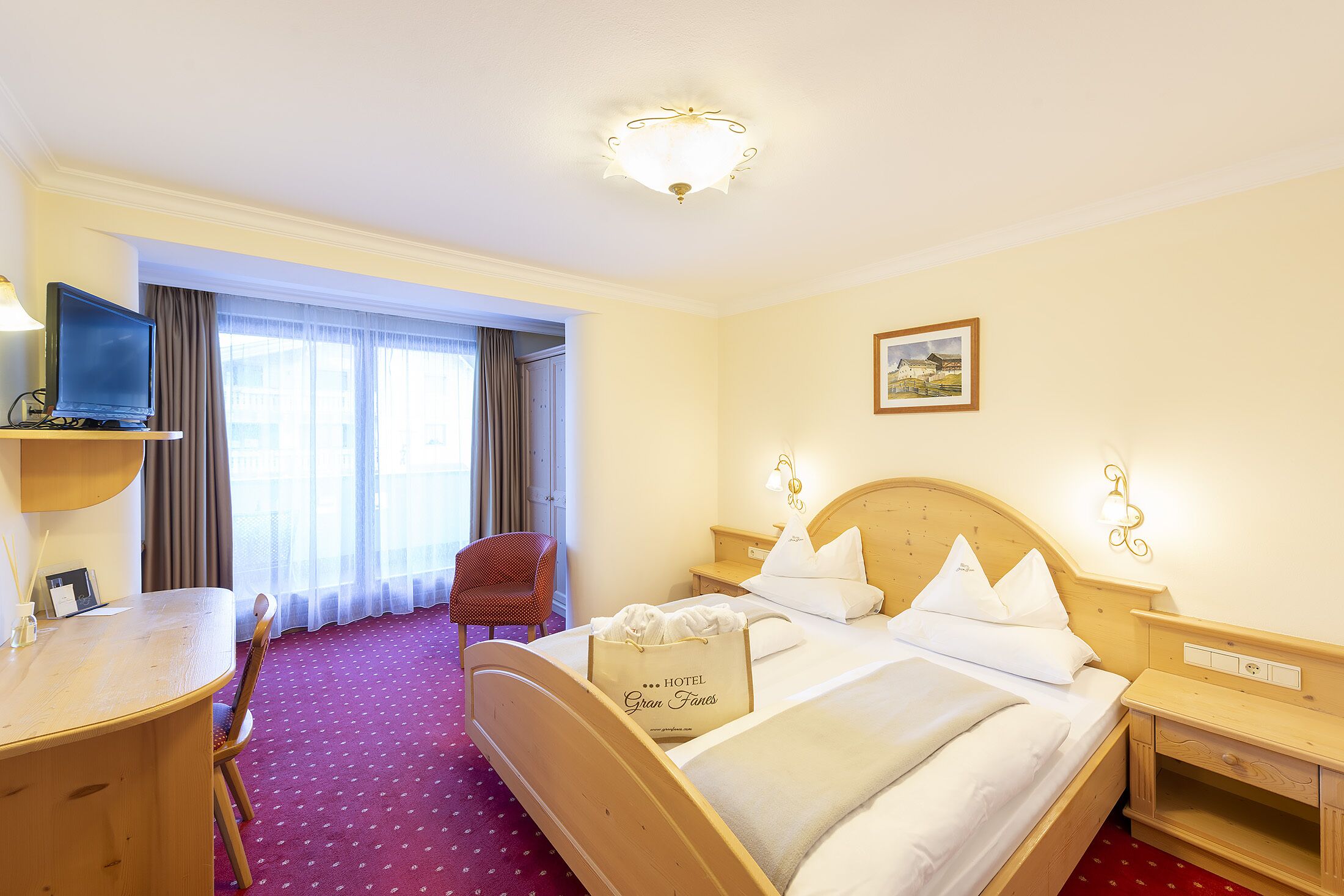 A hotel room with a bed, a desk, a chair, a television, and a window with curtains.