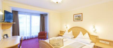 A hotel room with a bed, a desk, a chair, a television, and a window with curtains.