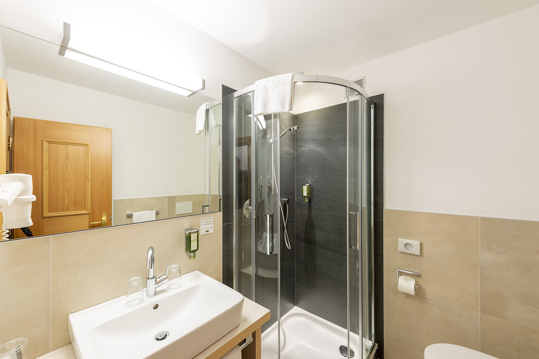 Un baño moderno con ducha envuelta en vidrio, un lavabo blanco y un armario de madera.