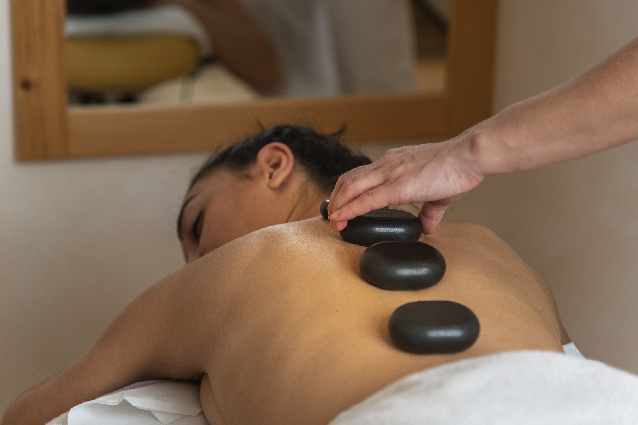 A person receiving a back massage with black stones.
