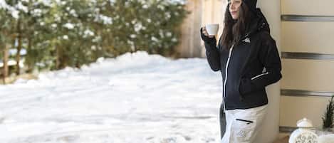 Una persona junto a una ventana con nieve afuera, sosteniendo una taza.