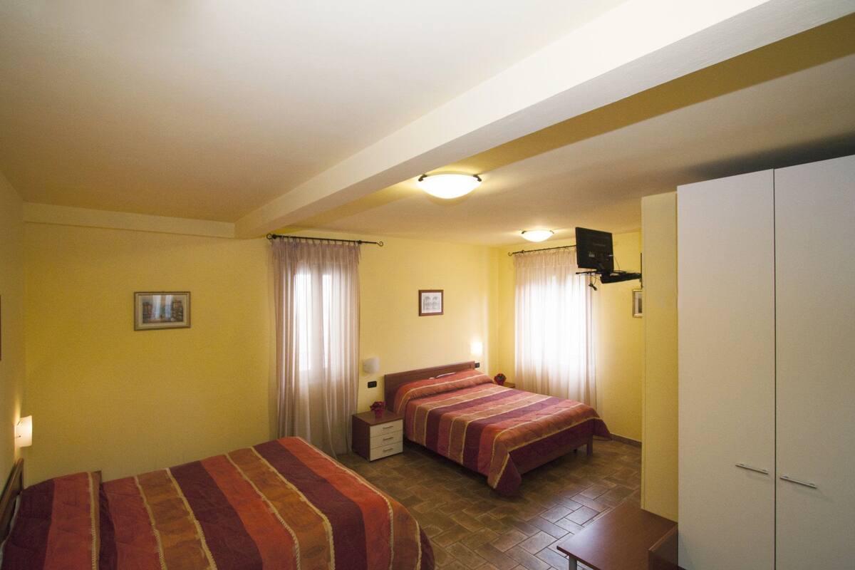 A hotel room with two beds, a wardrobe, a bedside table, a TV, and curtains.