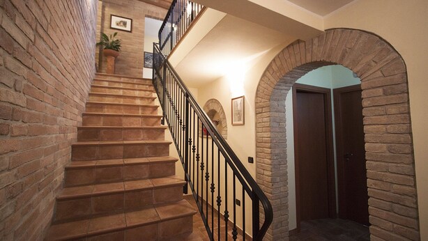 A staircase with a brick wall on one side and a stone archway on the other, leading to a door. - Camere Santucci (Assisi)