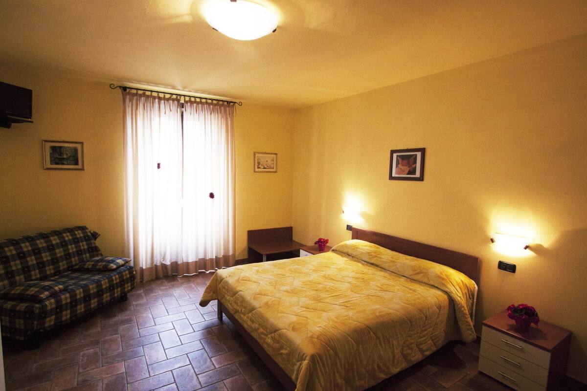 A hotel room with a bed, a sofa, a nightstand, and a window with curtains.