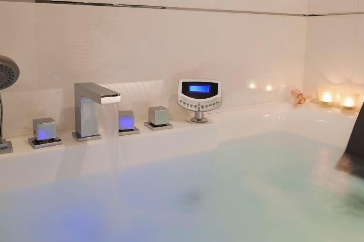 Un baño moderno con bañera, panel de control digital para la ducha y un juego de luces.