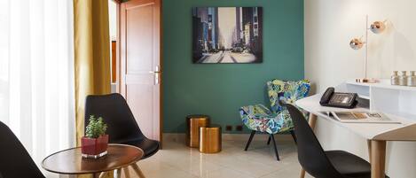 A modern hotel room with a teal accent wall, a cityscape painting, a desk with a telephone, and a chair with a colorful pattern.