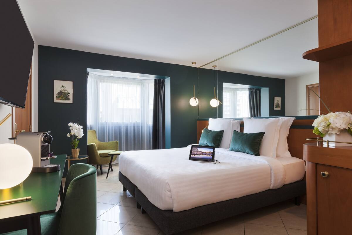 A hotel room with a large bed, a desk with a laptop, a chair, and a coffee machine.