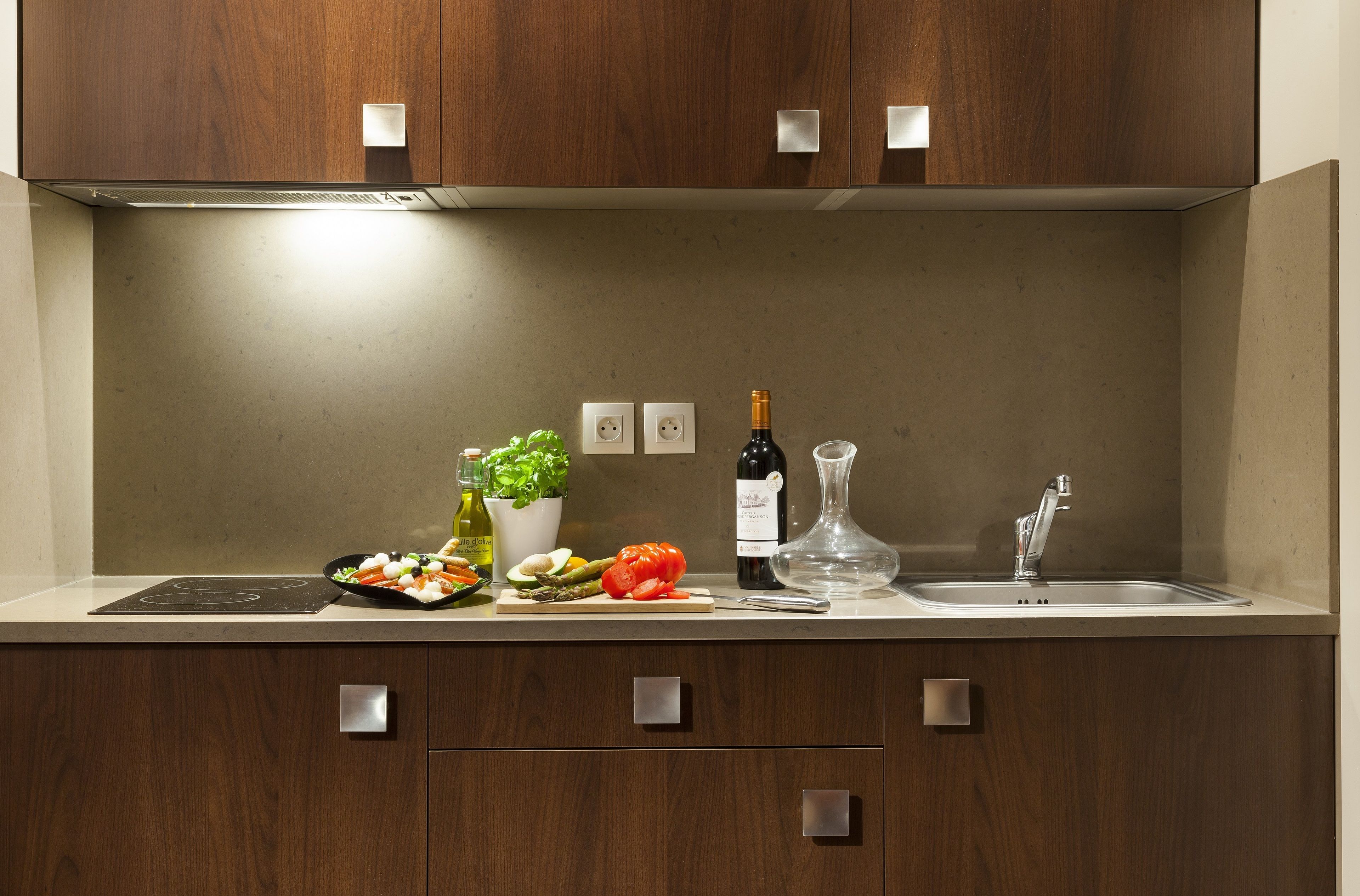 A modern kitchen with wooden cabinets, a built-in stove, a sink, and various kitchen items.