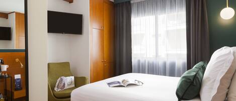 Une chambre d’hôtel avec un lit, une chaise, une télévision et une fenêtre avec des rideaux.