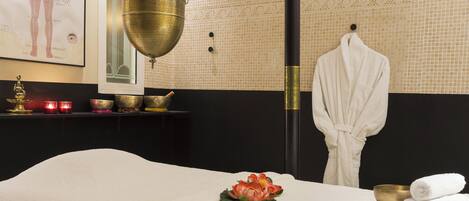 A massage room with a massage table, a decorative flower, a bowl, and a robe hanging on a hook.