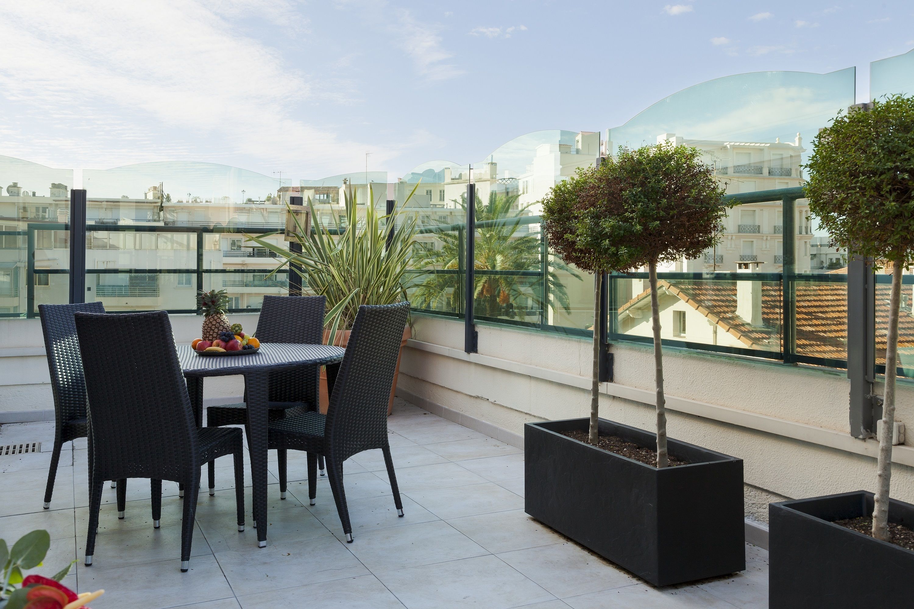 A rooftop terrace with a table and chairs, potted plants, and a city view.