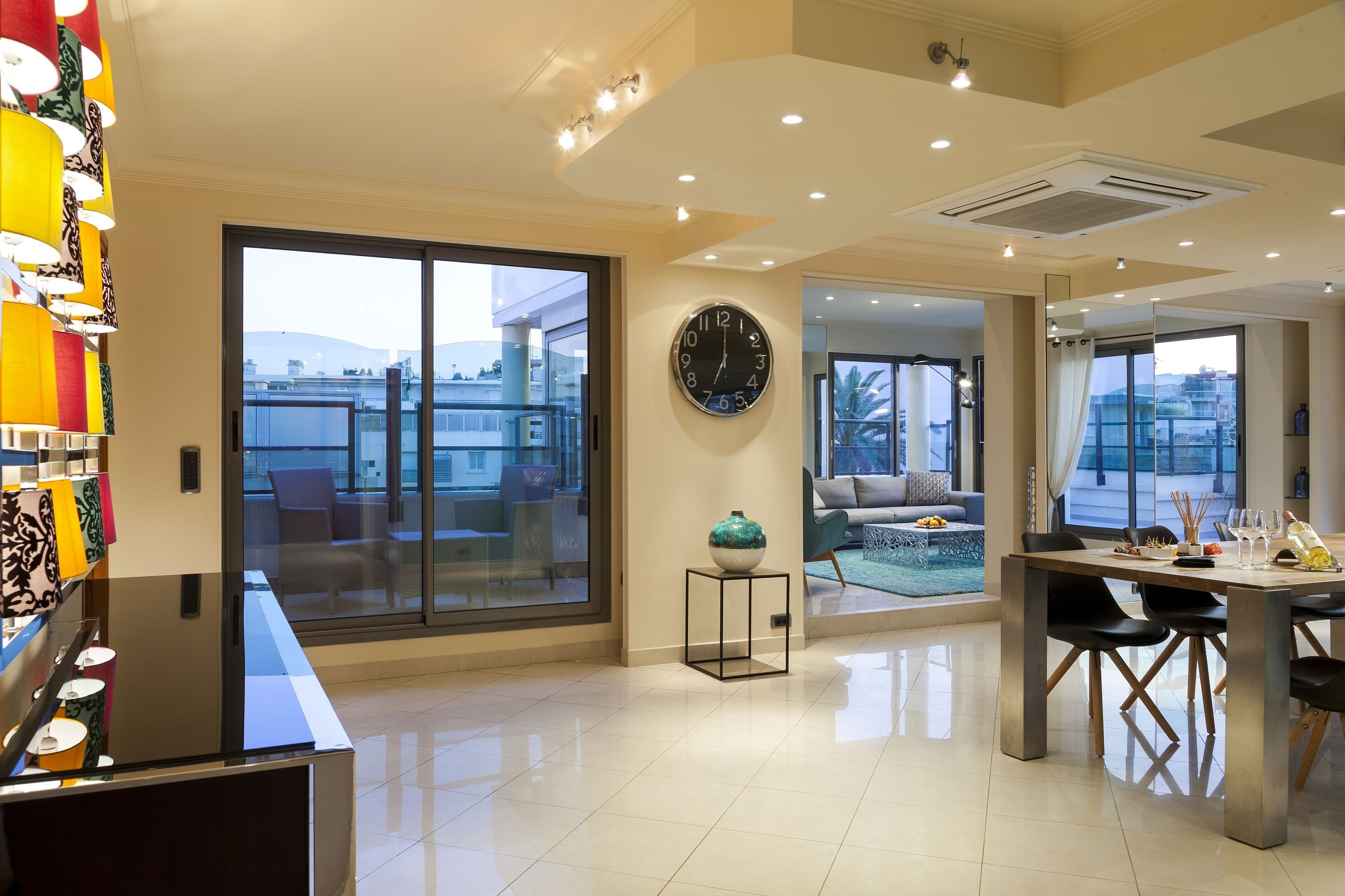 A modern hotel lobby with a large clock, a dining area, and a view of the cityscape through large windows.