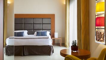 A modern hotel room with a large bed, a bedside table, a small table with a plant, and a window with curtains.