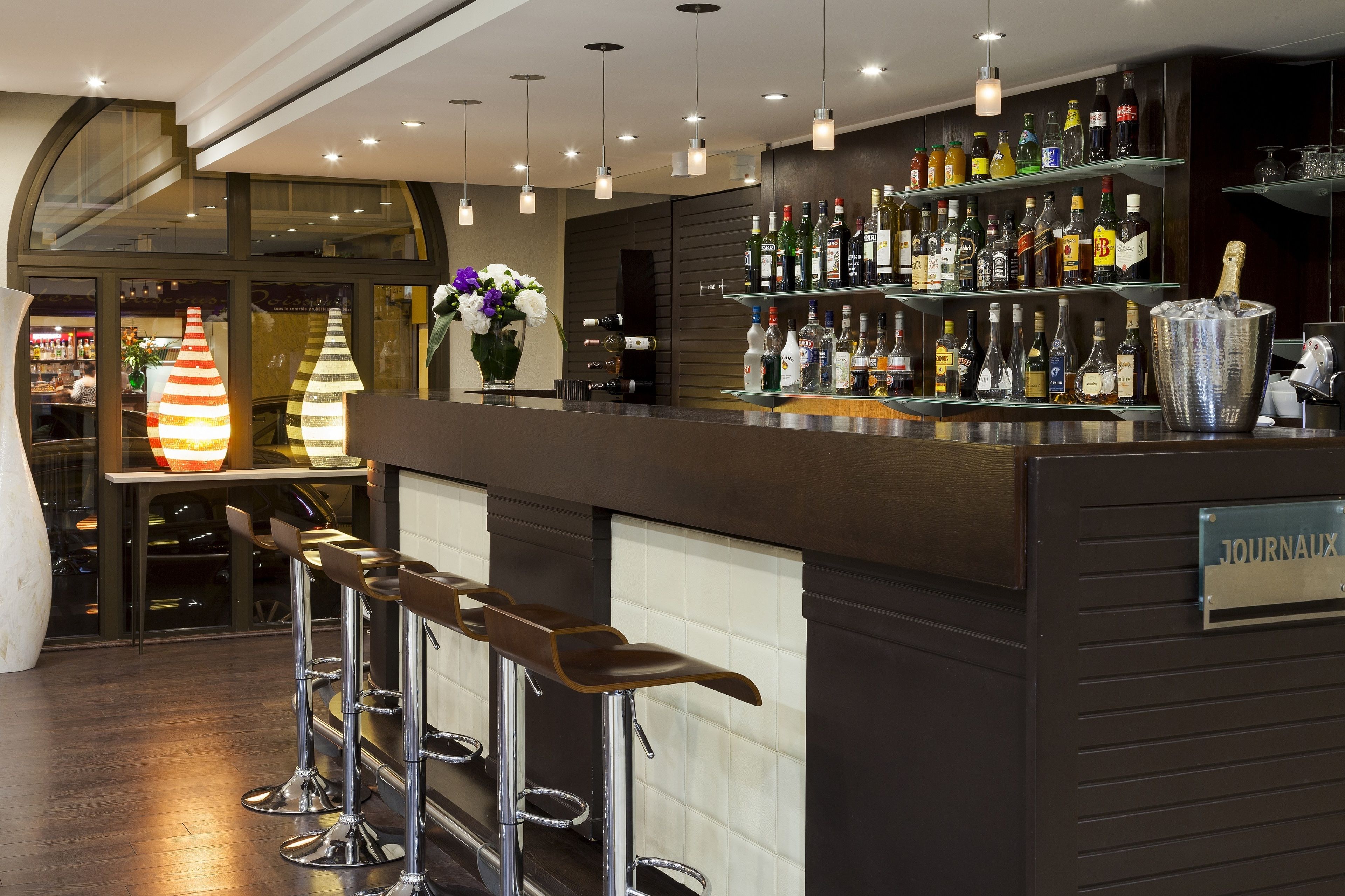 A bar area with stools, a variety of bottles, and a sign labeled "JOURNAUX".