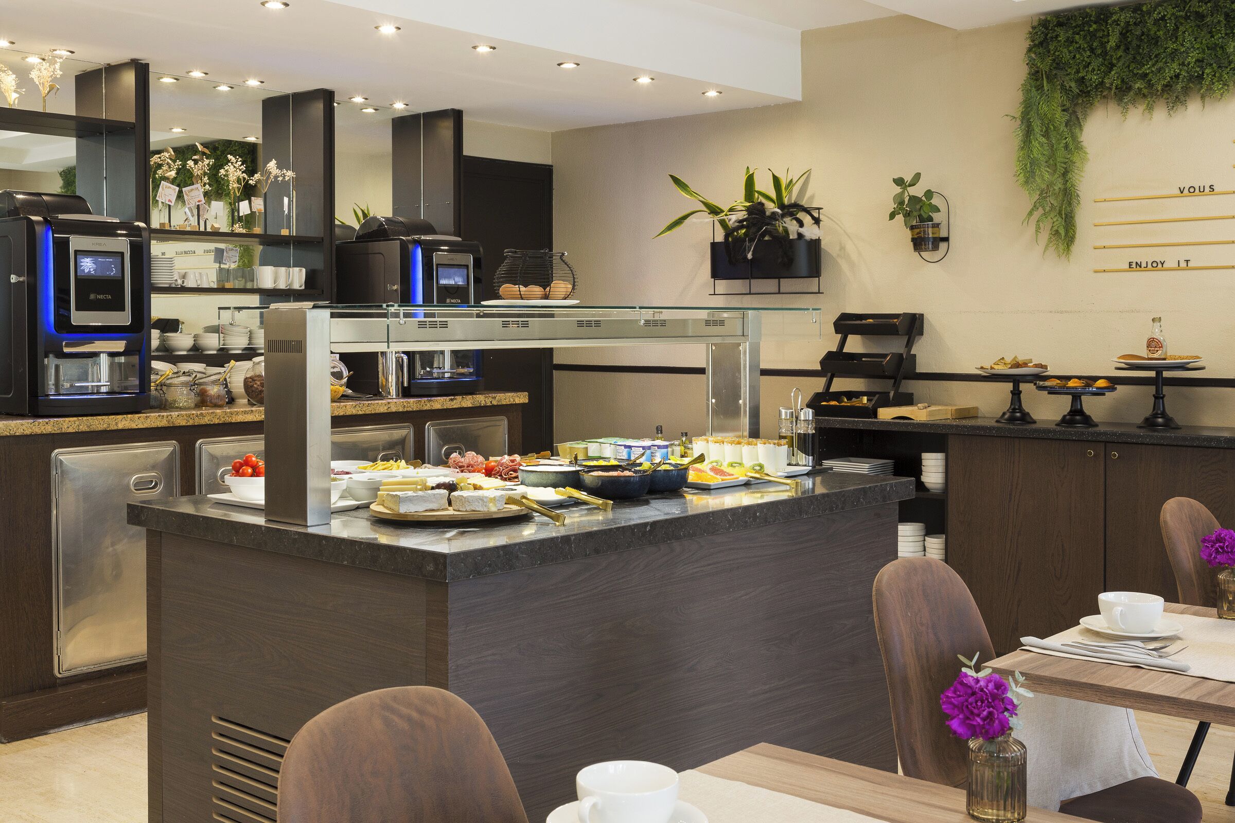 A modern kitchen with a buffet setup, including a coffee machine, a refrigerator, and various food items.
