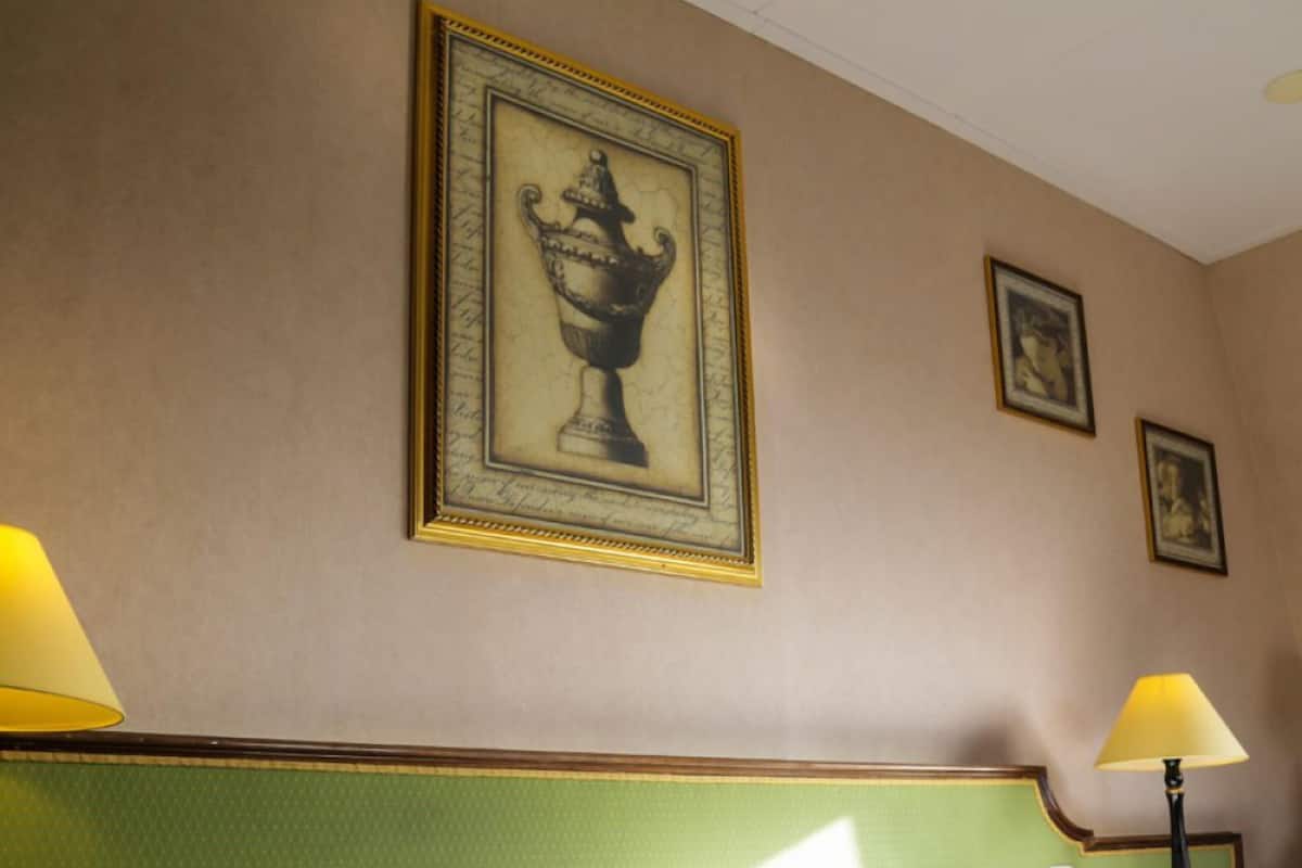 Een hotelkamer met een bed, twee bedlampen en lijstjes met kunstwerken aan de muur.