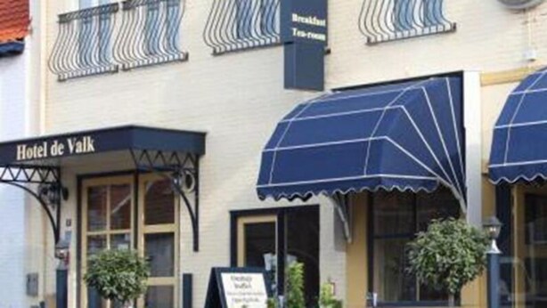 A building with a sign reading "Hotel de Valk" and a covered outdoor seating area. - Hotel De Valk (Westkapelle)
