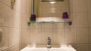 A bathroom with a white sink, a mirror, and a glass shelf with toiletries. - Hotel De Valk (Westkapelle)