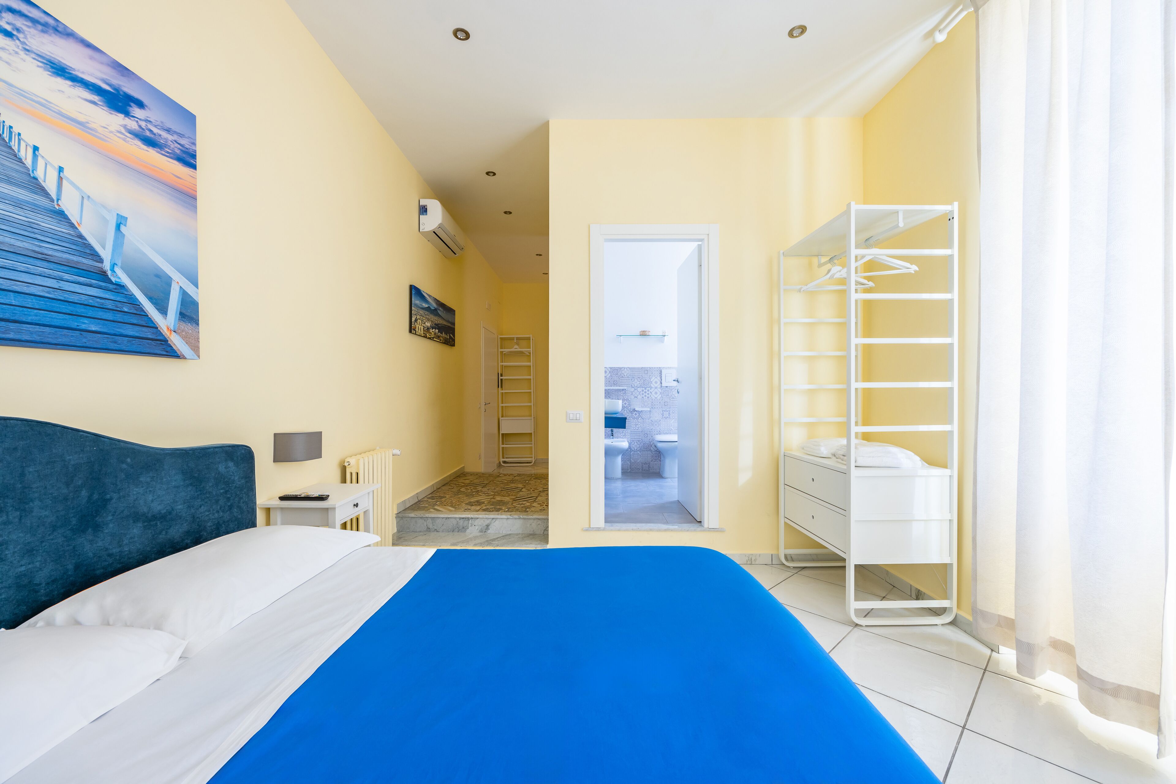 A hotel room with a bed, a walk-in closet, a bathroom, and a view of the sea.