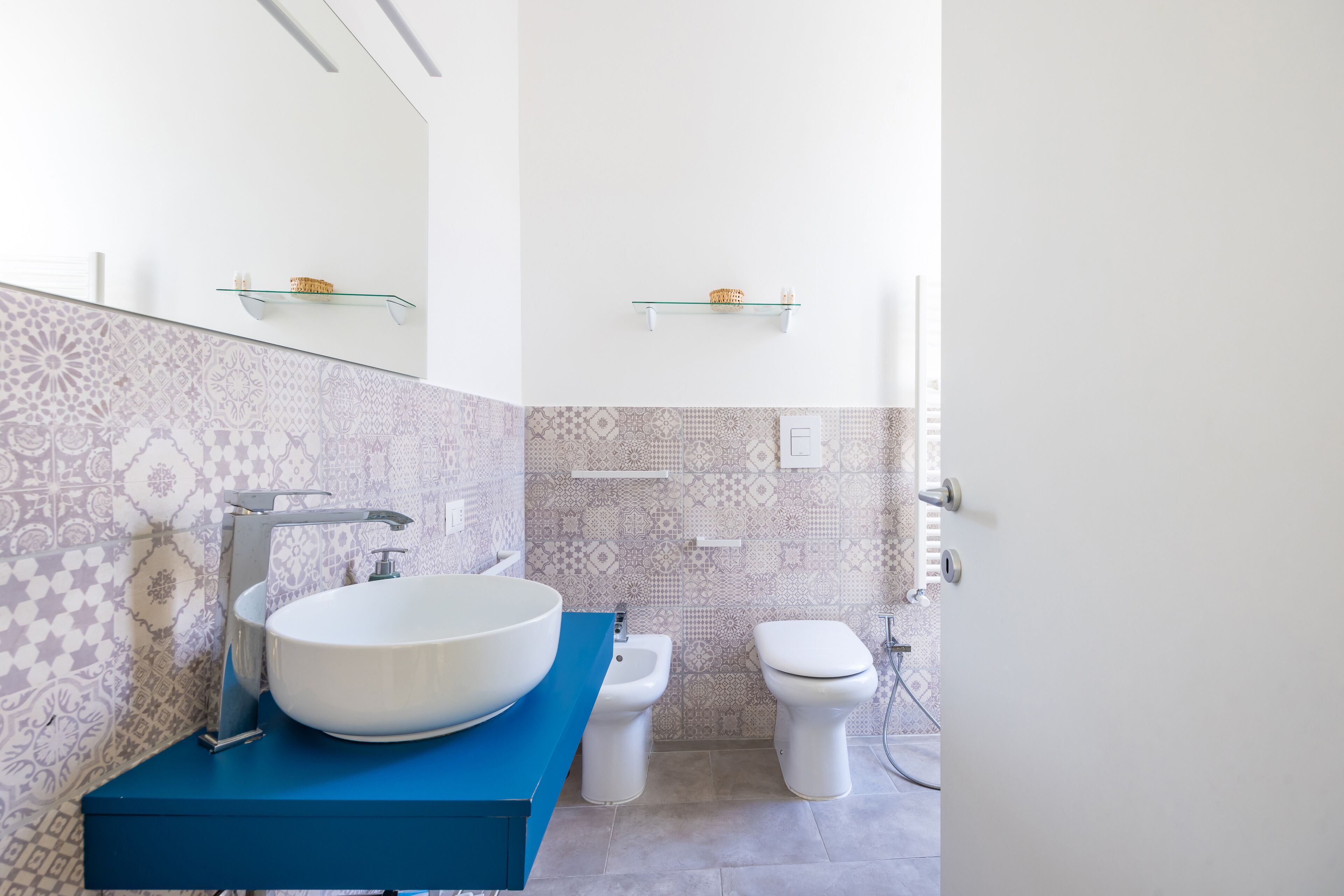 Un baño moderno con un lavabo blanco grande, encimera azul y un salpicadero de azulejos estampados.