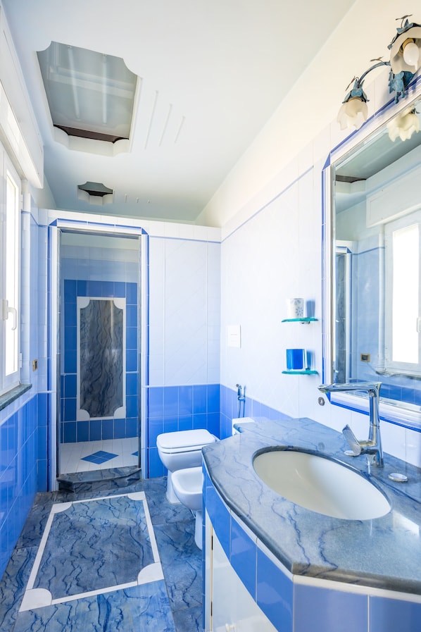 A bathroom with a blue and white color scheme, a large sink, and a shower area. - La Casa di Bruno Napoli (Naples)