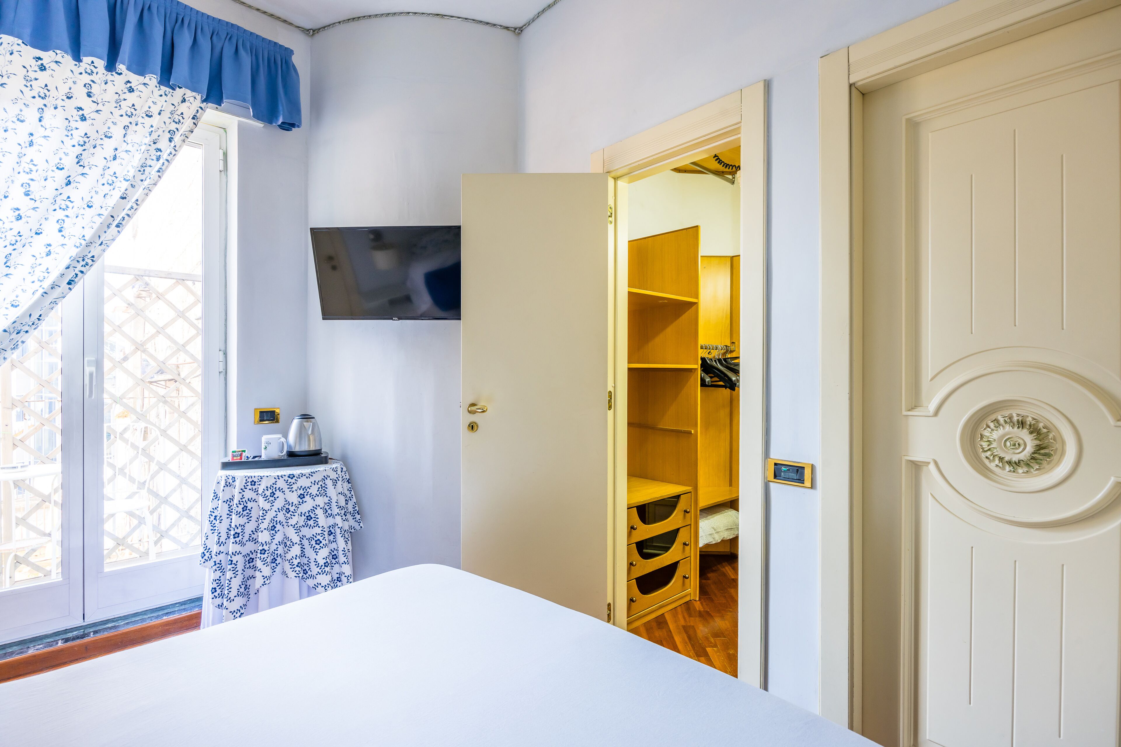 Een slaapkamer met een bed, een nachtkastje met waterkoker, een kledingkast en een televisie aan de muur.