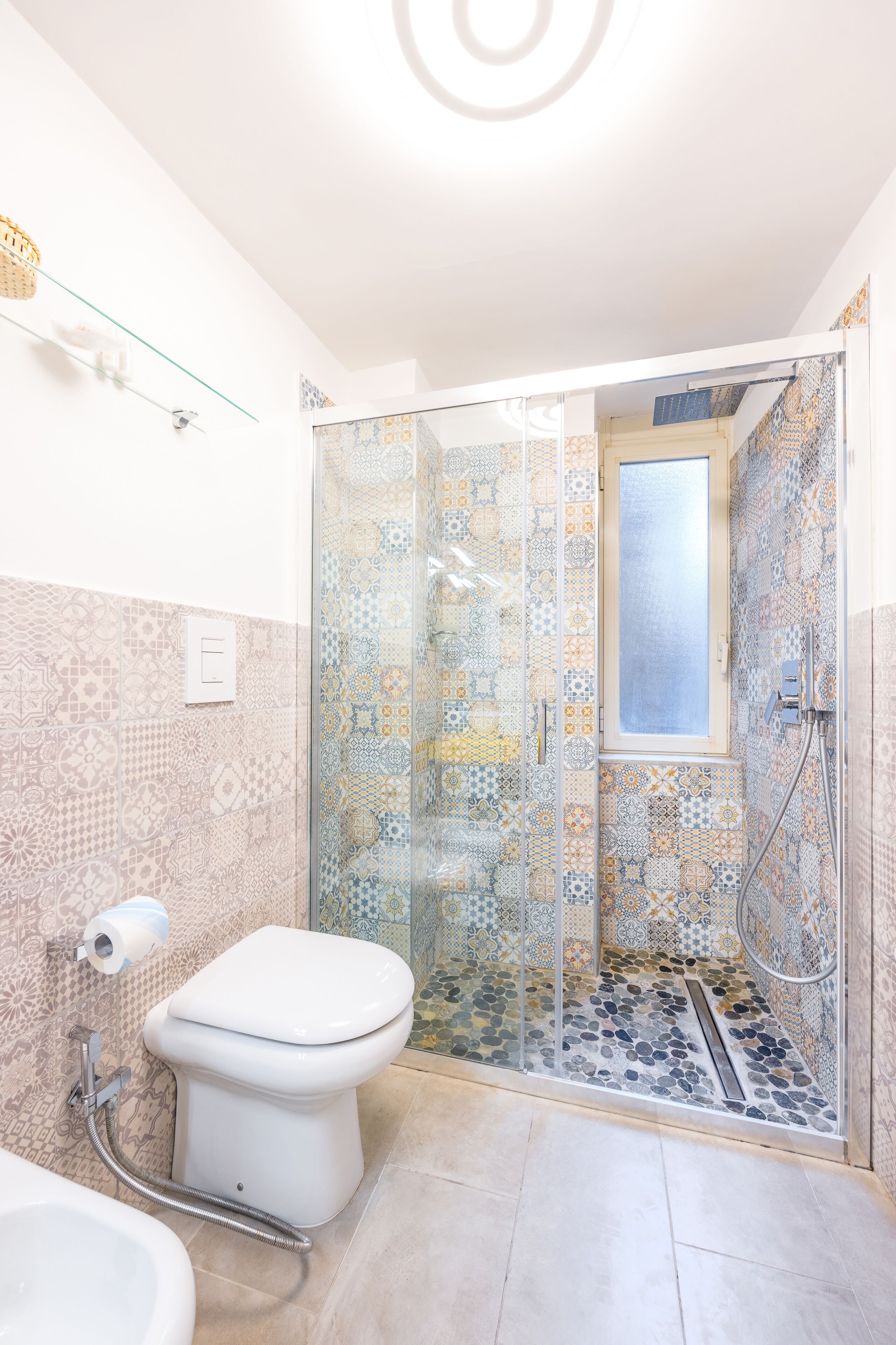 A bathroom with a glass-enclosed shower, patterned tiles, a toilet, and a bidet.