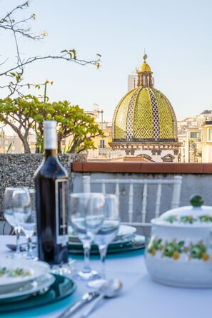 A dining table set with plates, glasses, and a bottle, overlooking a cityscape with a distinctive yellow-domed building. - La Casa di Bruno Napoli (Naples)