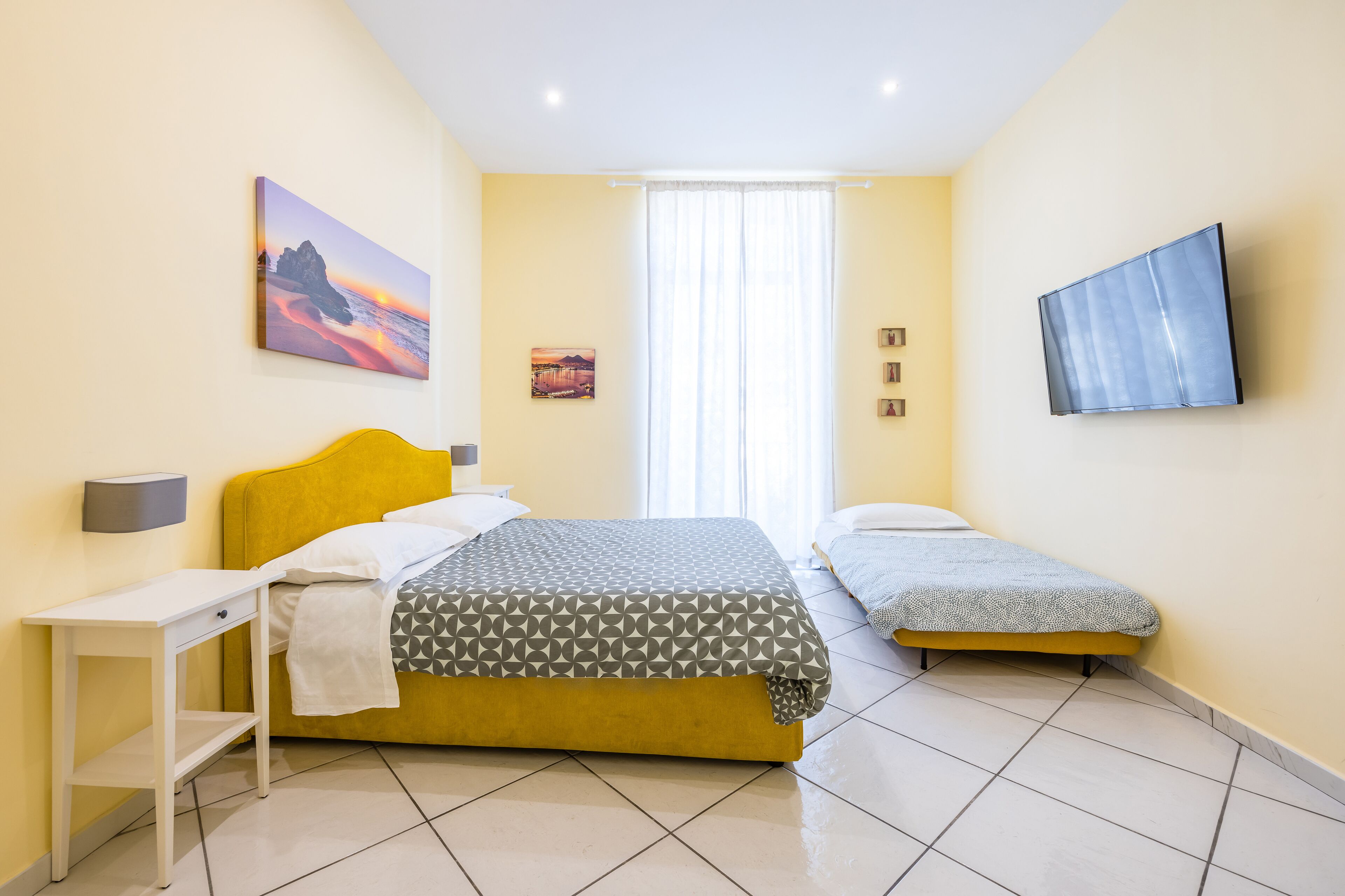 A bedroom with a bed, two bedside tables, a TV, and a window with curtains.