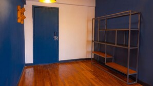 Una habitación con puerta azul, suelo de madera, estantería metálica y lámpara colgante.