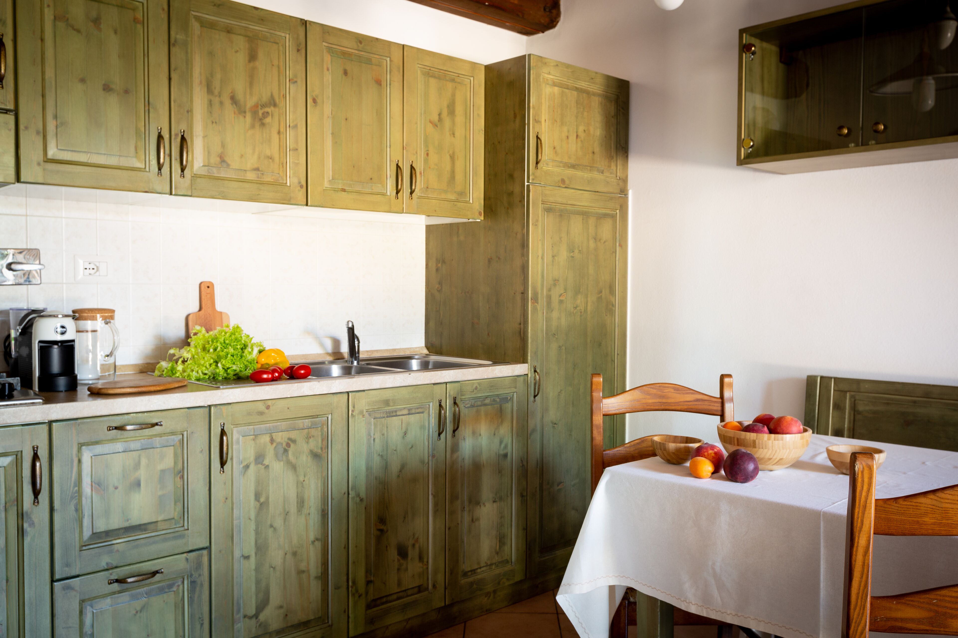 Een keuken met houten kastjes, een spoelbak, een koffiezetapparaat en een tafel met een schaal fruit.