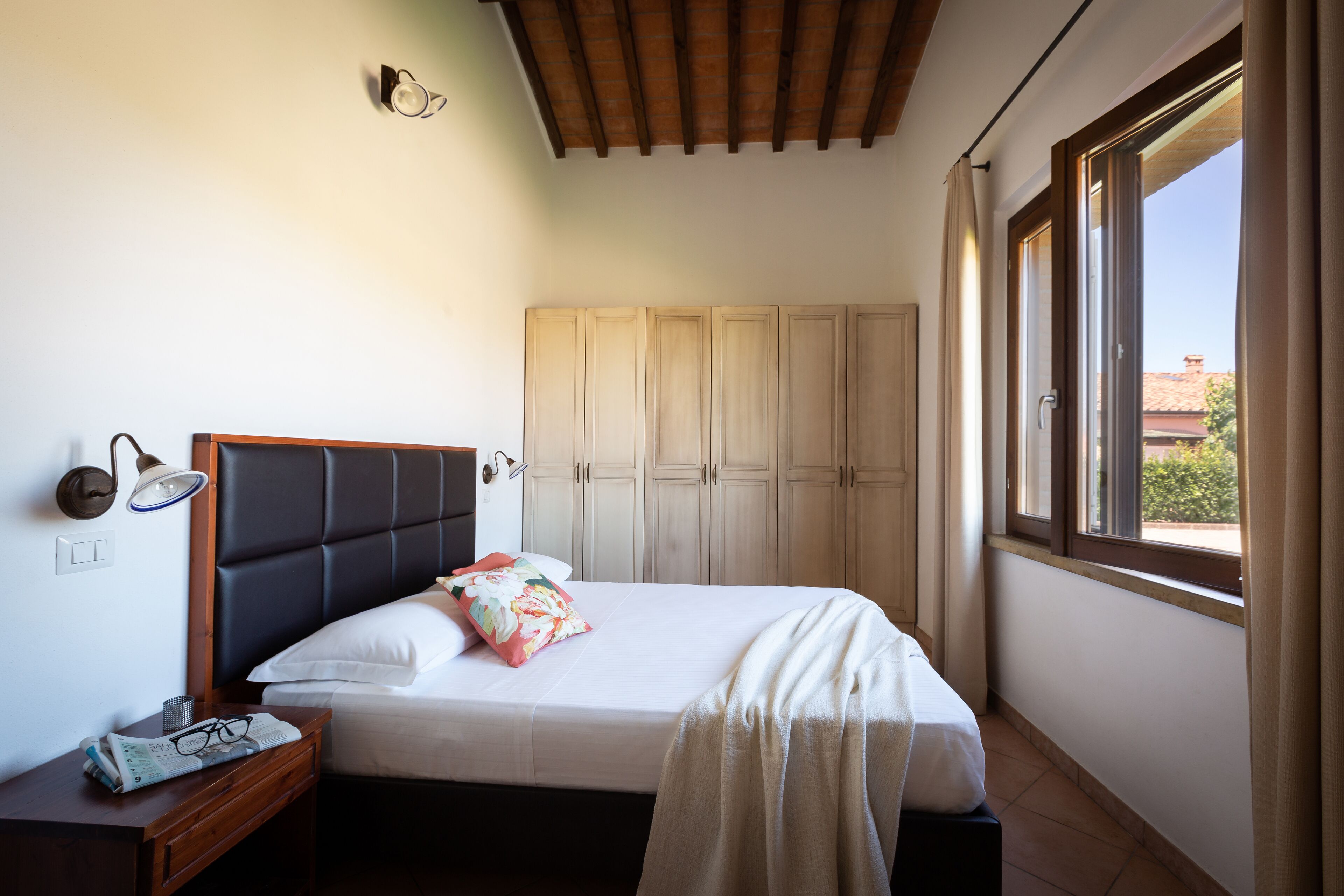 A bedroom with a bed, a nightstand, a wardrobe, and a window with curtains.