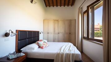 Un dormitorio con cama, mesita de noche, armario y ventana con cortinas.
