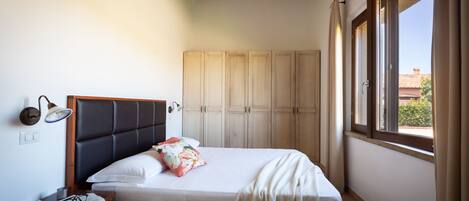 A bedroom with a bed, a nightstand, a wardrobe, and a window with curtains.
