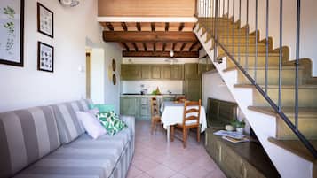 Un espacio de sala acogedor con un sofá, una mesa de comedor y sillas. Una escalera conduce a un nivel superior.