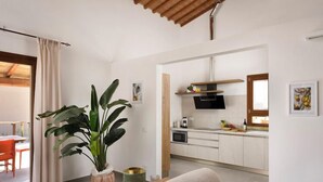 A modern living room with a sofa, a large potted plant, and a kitchen area with white cabinets and a microwave. - Borgo Verde (Rosignano Marittimo)