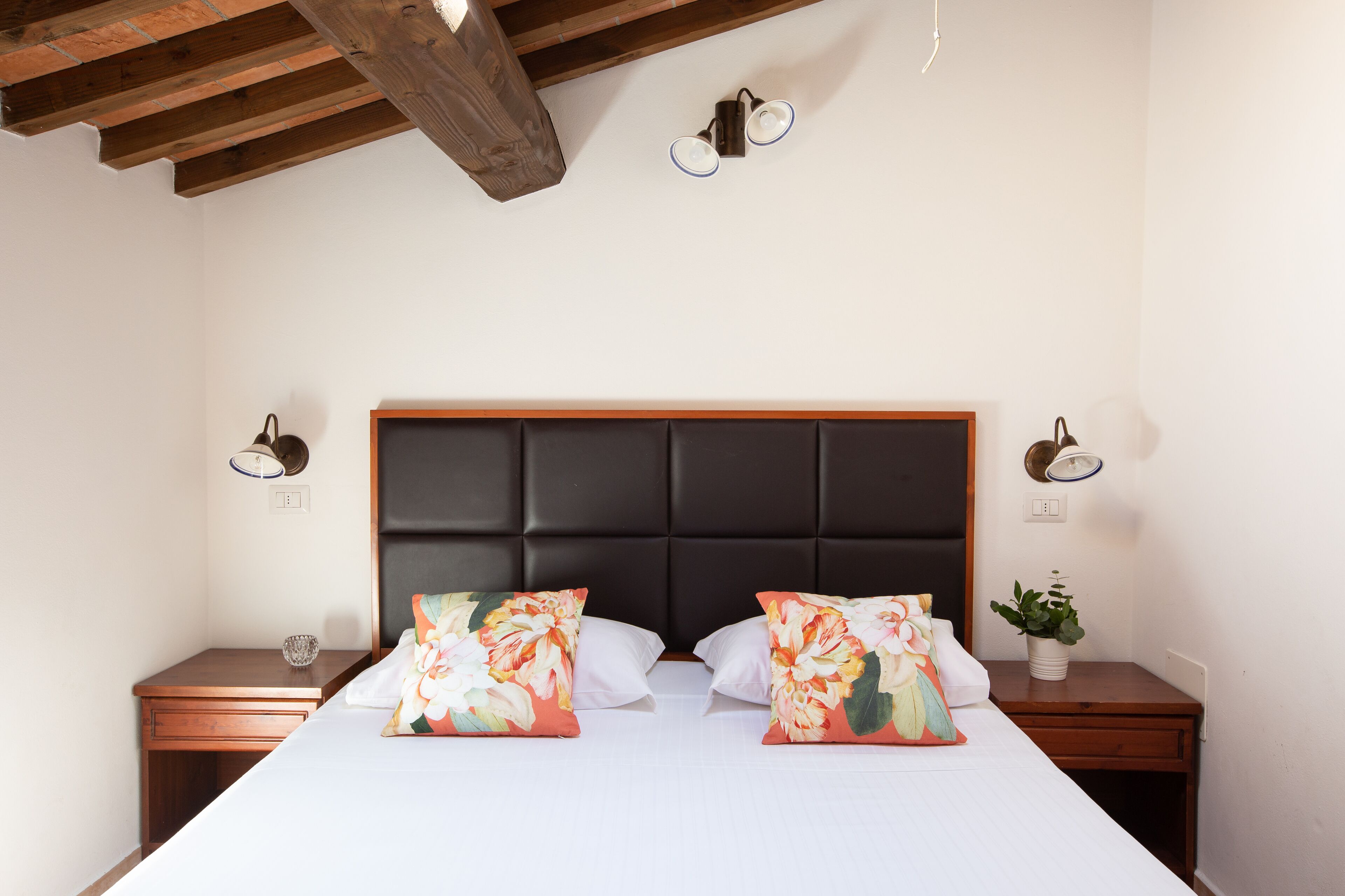 Quarto de hotel com uma cama grande, duas mesas de cabeceira, uma cabeceira de madeira e duas luminárias fixadas na parede.