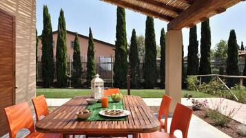 An outdoor patio with a wooden table and orange chairs, a lantern, and a bowl of fruit.