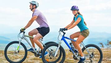 Deux personnes à vélo sur un sentier, avec une chaîne de montagnes en arrière-plan.