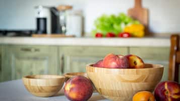 Cozinha com tigelas de madeira contendo frutas, uma cafeteira e uma fruteira no balcão.