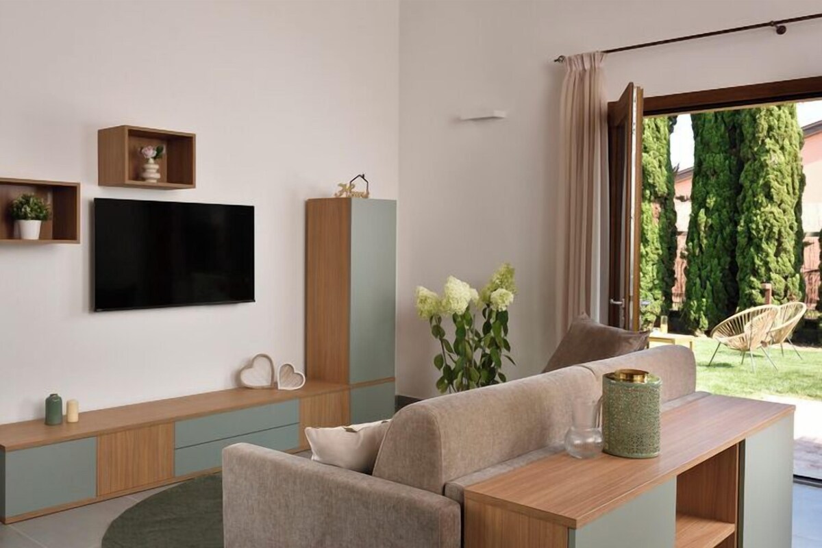 Un salon moderne doté d’un téléviseur à écran plat, d’un canapé, d’une table basse et offrant une vue sur un jardin grâce à une grande fenêtre.