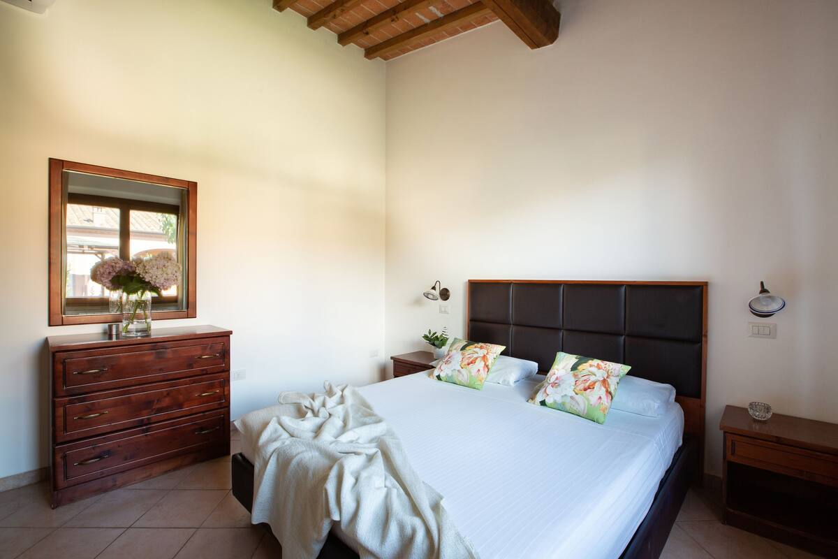 A bedroom with a large bed, wooden dresser, and a mirror.