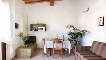 Un comedor con una mesa dispuesta para dos personas, un televisor sobre un mueble de madera y un sofá.