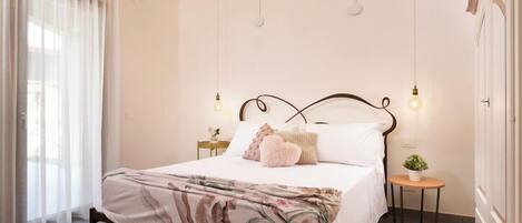 Un dormitorio con cama, mesita de noche, lámpara y ventana con cortinas.