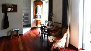 Een kamer met houten vloer, een eettafel met stoelen, een bank, een spiegel en een raam met gordijnen.