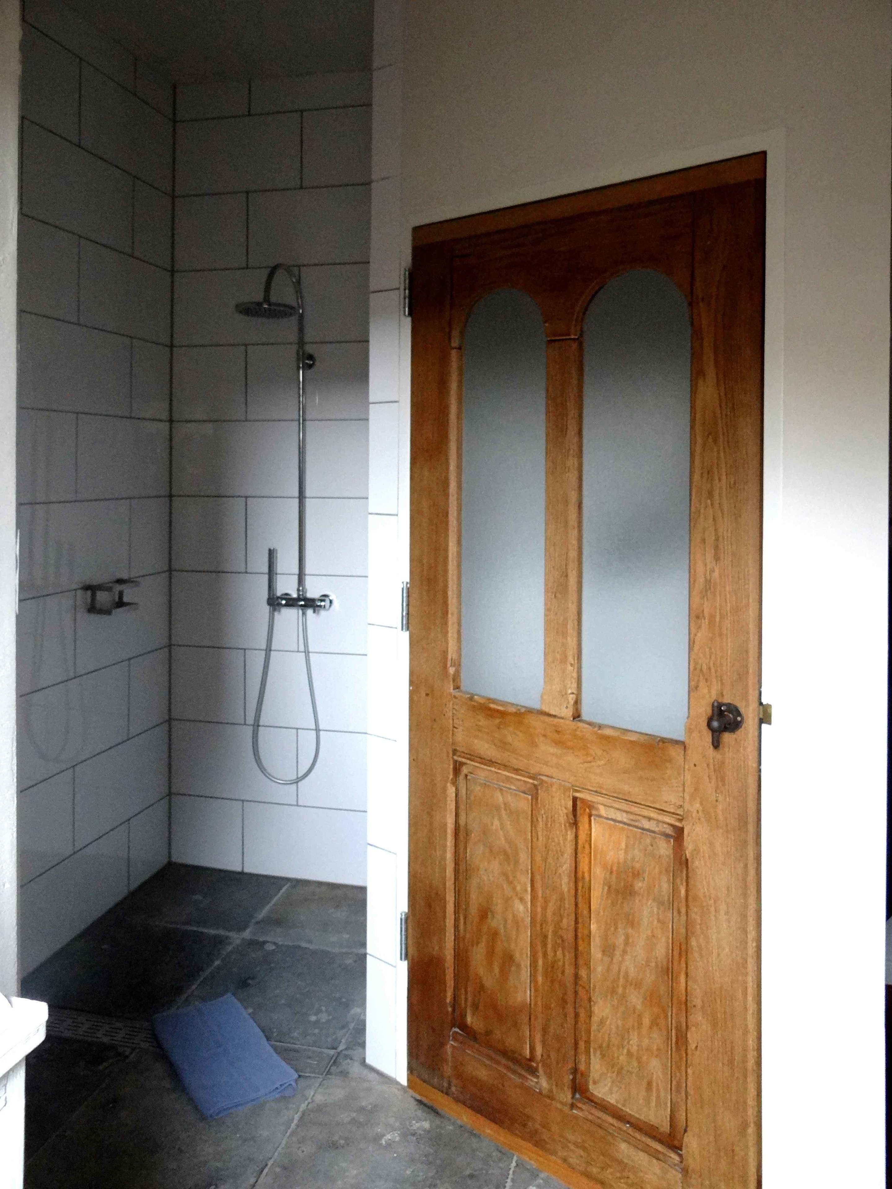 Ein Badezimmer mit Dusche, einer Holztür und einer blauen Matte auf dem Boden.